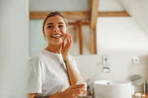 Woman smiling and applying moisturizer after microneedling treatment in Dallas, TX